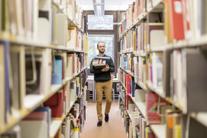 Generisches Bild einer Bibliothek mit einer Person, die Bücher trägt.