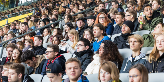 Studierende des ersten Semesters sitzen bei der Erstsemesterbegrüßung auf den Rängen im Stadium.