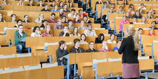 Eine Dozierende steht vor Studierenden in der Vorlesung im Hörsaal. 