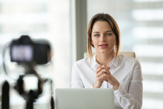 Frau bei Videoaufnahme Eine Frau sitzt mit ihrem Laptop vor einer Kamera und nimmt ein Video auf.