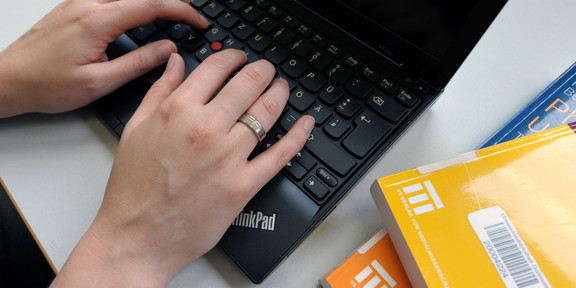 Lernen mit dem Laptop Eine Studentin tippt an einem Laptop und gelbe Bücher legen daneben.