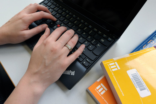 Eine Studentin tippt an einem Laptop und gelbe Bücher legen daneben.